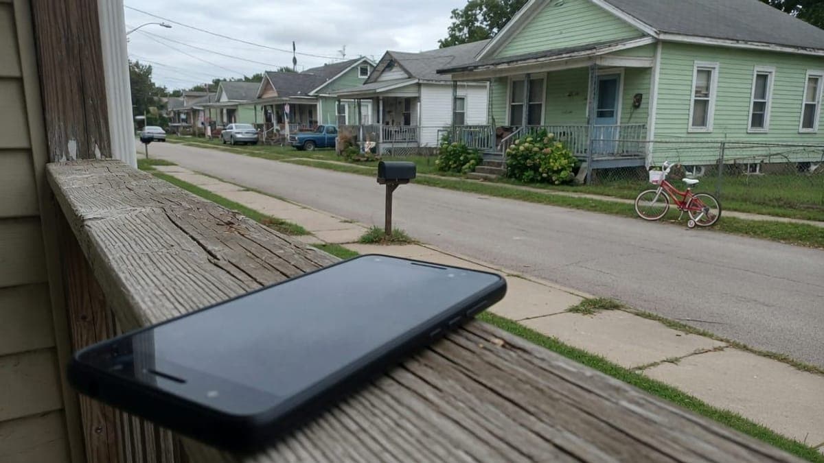 Telefono appoggiato alla ringhiera di una veranda, con una casa verde e una bicicletta rossa dall'altra parte della strada.