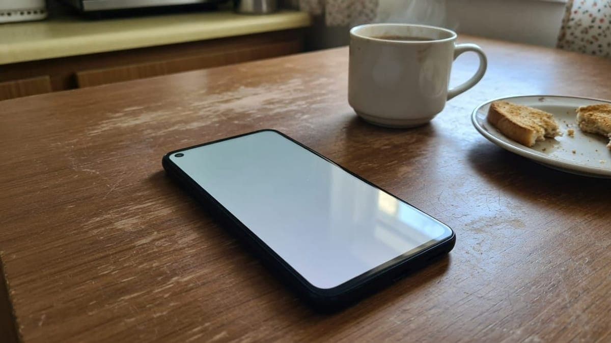Telefono Android con lo schermo rivolto verso l'alto su un tavolo di legno, accanto a una tazza di caffè e a una fetta di pane tostato.
