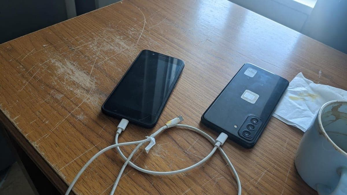 Due telefoni scuri su un tavolo di legno segnato, con un cavo USB-C bianco arrotolato fra loro.