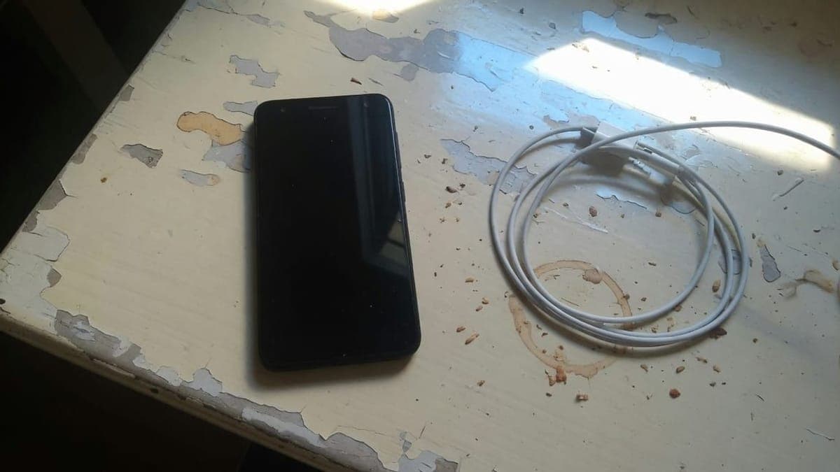 Telefono scuro e cavo bianco arrotolato su un tavolo segnato, con l'impronta di una tazza.