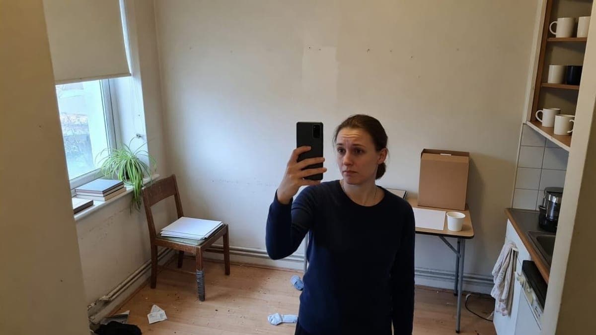 Donna che tiene un telefono per fotografarsi davanti a una parete bianca della cucina.