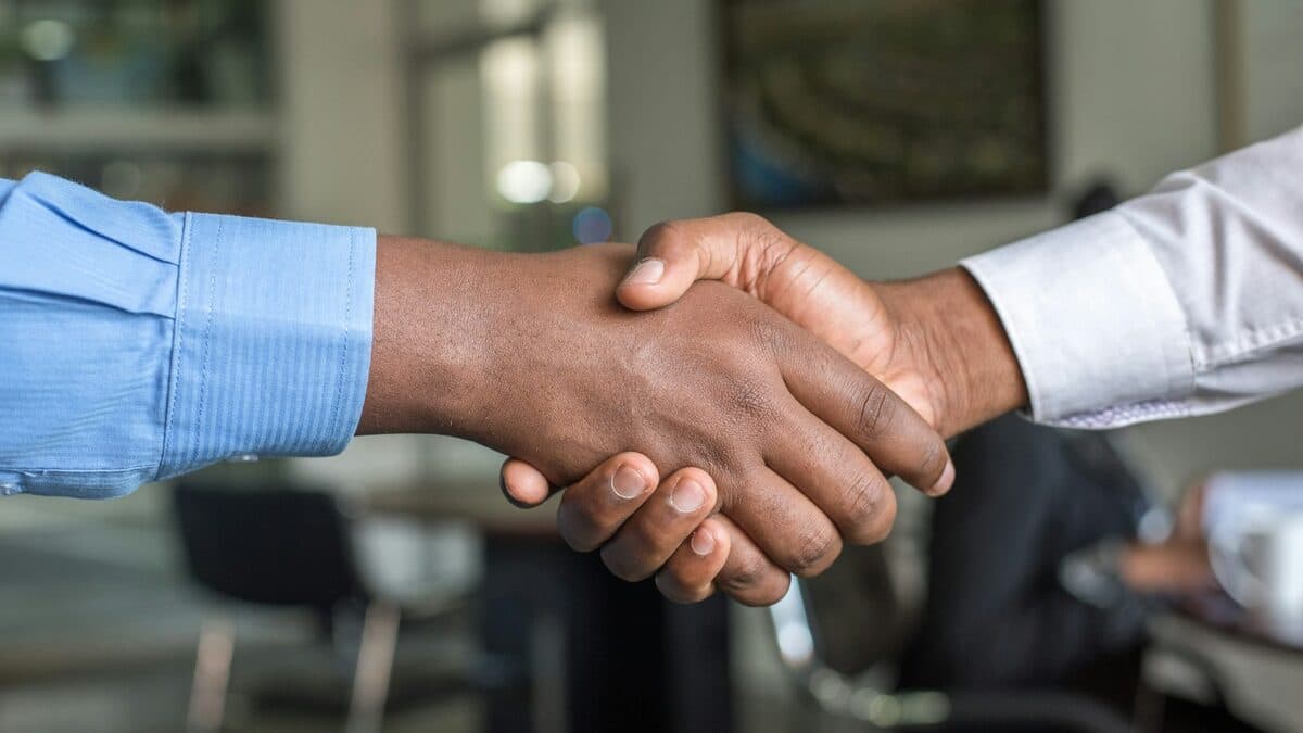 Due persone con camicie azzurra e bianca si stringono la mano in un ufficio.