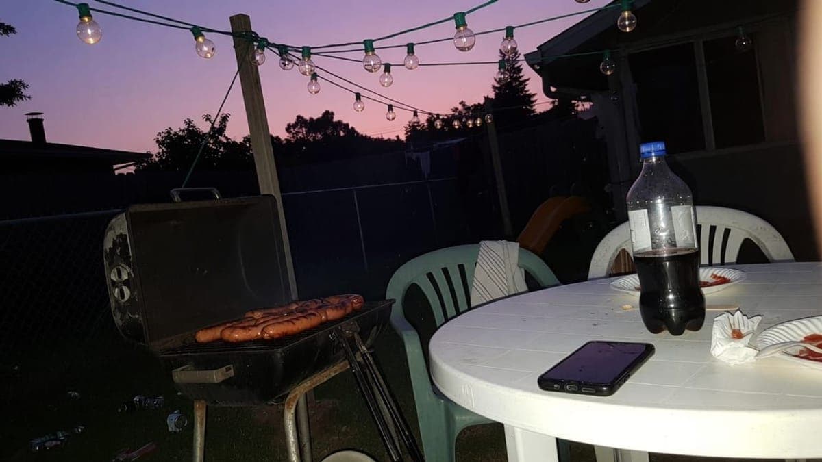 Hot dog su una griglia a carbone al tramonto, con lucine sospese e un telefono sul tavolo.