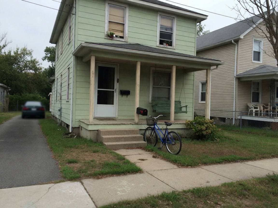Pale green house with a porch, a black mailbox, and a blue bicycle by the steps.