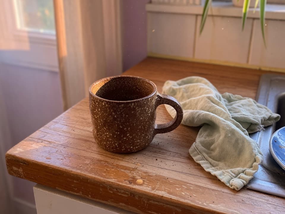 Handmade speckled ceramic mug on a worn kitchen counter, the kind of photo people mark before posting.